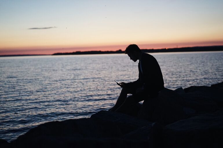 Person sitting on rocks with the sea in the background at sunset - Cookiebot
