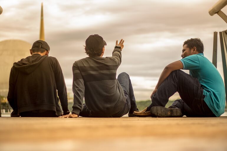 Three people sitting on the ground chatting outside - Cookiebot